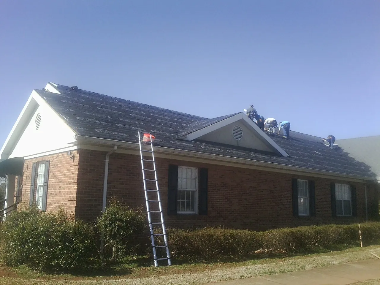 Crew tearing shingles off a brick ranch roof with a ladder set — Metal Roof Repair work by our crew in Falcon