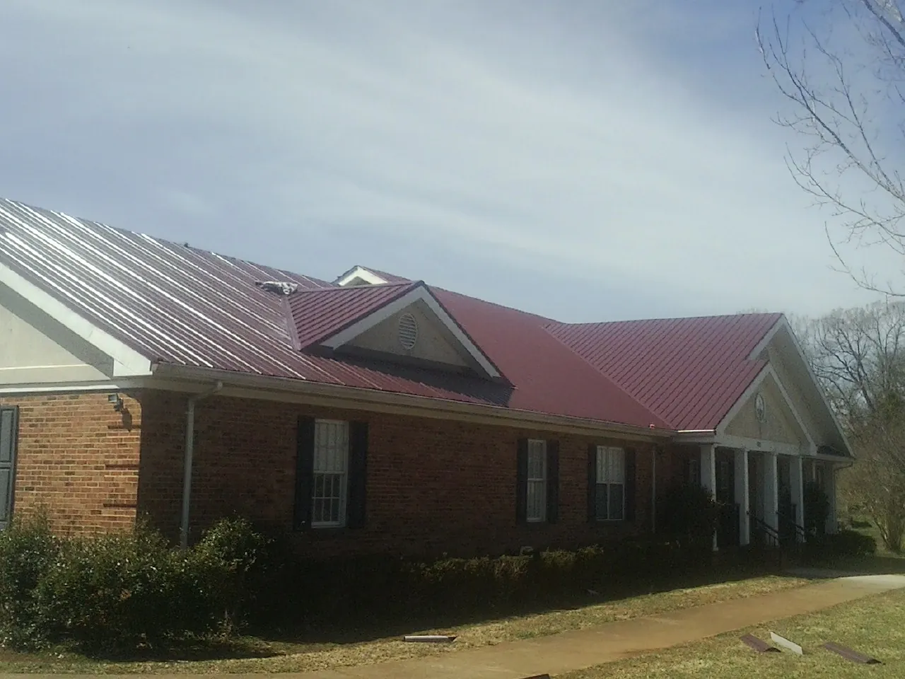 Red metal roof with gabled entries on a long brick building, from a Hail Damage Roof Repair job in Falcon