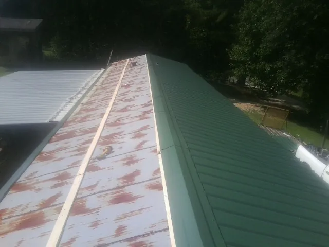 Old rusted panels beside newly installed green metal roofing — Wind Damage Roof Repair by Roofing Brothers in Falcon