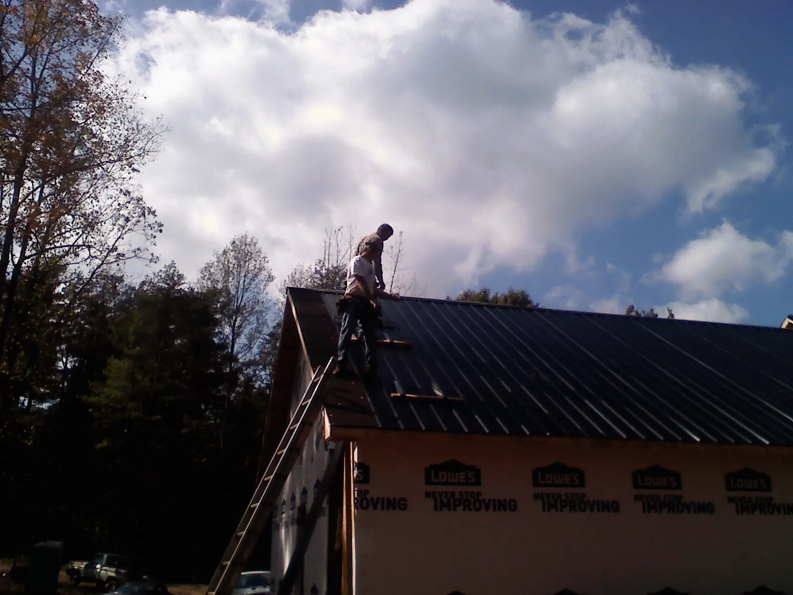 Roofer fastening dark metal panels high against a cloudy sky, from a Roof Inspection job in Falcon